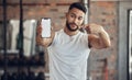 Athlete making a facial expression holding his phone. Fit young man showing his mobile device screen in the gym