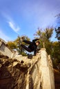 Athlete man, brave young guy in sportswear flips over wall, practice Parkour in public park over sky view in motion blur