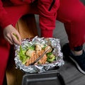 Athlete Man eating omega-rich seafood, red fish with vegetables wrapped in foil. Takeaway food concept. Square format or