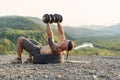 Athlete man making exercises with dumbbells outdoors on the mountain hill at sunset background. Royalty Free Stock Photo