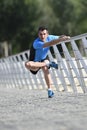 Athlete man stretching legs warming up muscles before running workout leaning on railing city urban park Royalty Free Stock Photo