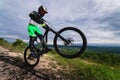 athlete performs a stunt while standing on a wheelie on a rock, overlooking green forests and mountains. cycling extreme