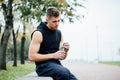 Athlete resting on bench in park after running with bottle of water. Rest a hard workout. Royalty Free Stock Photo