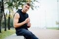 Athlete resting on bench in park after running with bottle of water. Rest a hard workout. Royalty Free Stock Photo