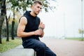 Athlete resting on bench in park after running with bottle of water. Rest a hard workout. Royalty Free Stock Photo