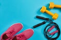 Athlete`s set with female clothing, dumbbells and jump rope on bright blue background