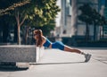 Athlete slim blonde woman fitness trainer in blue sportswear does workout push-ups from bench on city street