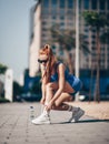 Athlete slim blonde woman trainer runner in blue sportswear ties her sneakers before workout on city street