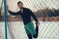 Athlete stretching quadriceps on the fence on a snowy day