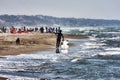 An athlete walks among the foam of the waves shore with his kite surfing board at Roman beach crowded by bathers and people Royalty Free Stock Photo