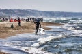 Athlete walks among the foam of the waves shore with his kite surfing board at Roman beach crowded by bathers and people Royalty Free Stock Photo