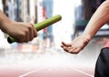 Athletes passing the baton during relay race against city buildings Royalty Free Stock Photo
