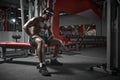 Athletic african american guy in headphones with phone using sport app sitting on sports bench during training in gym