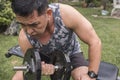 An athletic asian guy in his 50s exercising outdoors. Doing concentration bicep curls on a bench. Arm workout Royalty Free Stock Photo