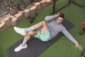 An athletic asian man does oblique floor crunches with one knee up lying on a black mat. Working out his midsection and core at