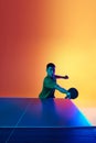 Athletic Asian man playing ping pong in neon light against warm yellow gradient background. Dynamic gel portrait.