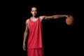 Athletic basketball player in uniform holding ball on black