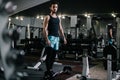 Athletic bearded young man with muscular wiry body wearing sportswear posing in modern dark gym.