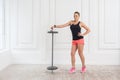 Athletic beautiful woman standing, holding barbell and looking at camera with confident expression.