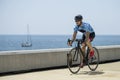 Athletic biker riding a bike in the street next to the sea. Fit cyclist training wearing helmet and sunglasses outdoors.