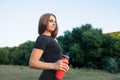 athletic blonde girl looks away and rests after a hard workout in the park holding a red bottle of water in her hands Royalty Free Stock Photo