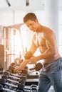 Athletic bodybuilder man lifting dumbbell from rack in gym and fitness club