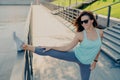 Athletic brunette woman stretches legs wears sunglasses t shirt leggings and sneakers has slim figure prepares for workou outdoors Royalty Free Stock Photo