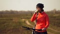 Athletic Caucasian woman eats protein bar ride on mountain bike on nature. Young sporty woman athlete in helmet resting while