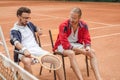 athletic friends with wooden rackets sitting on chairs after training