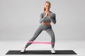 Athletic girl doing exercise for glutes with resistance band on gray background. Fitness woman working out