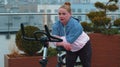 Athletic girl performing aerobic riding training exercises on cycling stationary bike on house roof