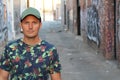 Athletic guy in a floral tee shirt and a baseball cap on urban background with copy space Royalty Free Stock Photo