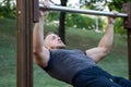 Athletic guy trains in the fresh air and performs lying down pull ups bar exercises Royalty Free Stock Photo