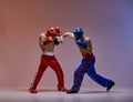 Athletic guys fighting, wearing boxing gloves on red blue studio background with copy space, mixed fight concept