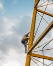 Athletic Hispanic man with the sky in the background climbing a metal structure. Young man dressed in urban clothes and a yellow