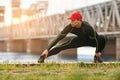 Athletic man doing stretching exercises, outdoor. Active male working out outside on the background of the bridge