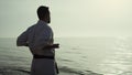 Athletic man honing karate technique enjoying sunset on beach back view