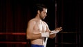 Athletic man, standing in boxing ring, wrapping hands with long white rope wrap around hand slowly, before practicing boxing at