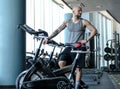 Portrait of a bald athletic man with a tattoo on his hand standing next to a exercise bike in the modern fitness club