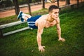 Athletic man during workout in park. Fitness personal trainer doing pushups on grass. Cross-fit training concept