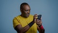 Athletic mature african american man in studio on blue background looking at mobile phone screen pensive male athlete