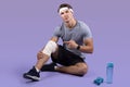 Athletic millennial man having sports injury, pointing at his sprained bandaged knee over lilac studio background Royalty Free Stock Photo