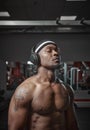 Athletic muscular african american man in wireless headphones listening music with closed eyes during training in gym Royalty Free Stock Photo