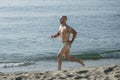 Athletic muscular man in swimwear running next to the sea. Professional male athlete training in speedo at the beach.