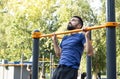 Athletic muscular sportsman trains on the horizontal bar in the city park