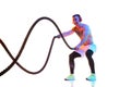 Athletic muscular young man in headphones training shitless with battle rope against white studio background in neon Royalty Free Stock Photo