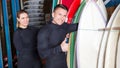 Athletic young people in wetsuits standing with surfboards