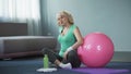 Athletic senior woman sitting on yoga mat and massaging her back, lumbago