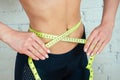 Athletic and sexy healthy woman measures waist measurement with measuring tape in a gym on a white background. the