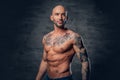 Athletic shaved head male with tattoos on his torso posing over